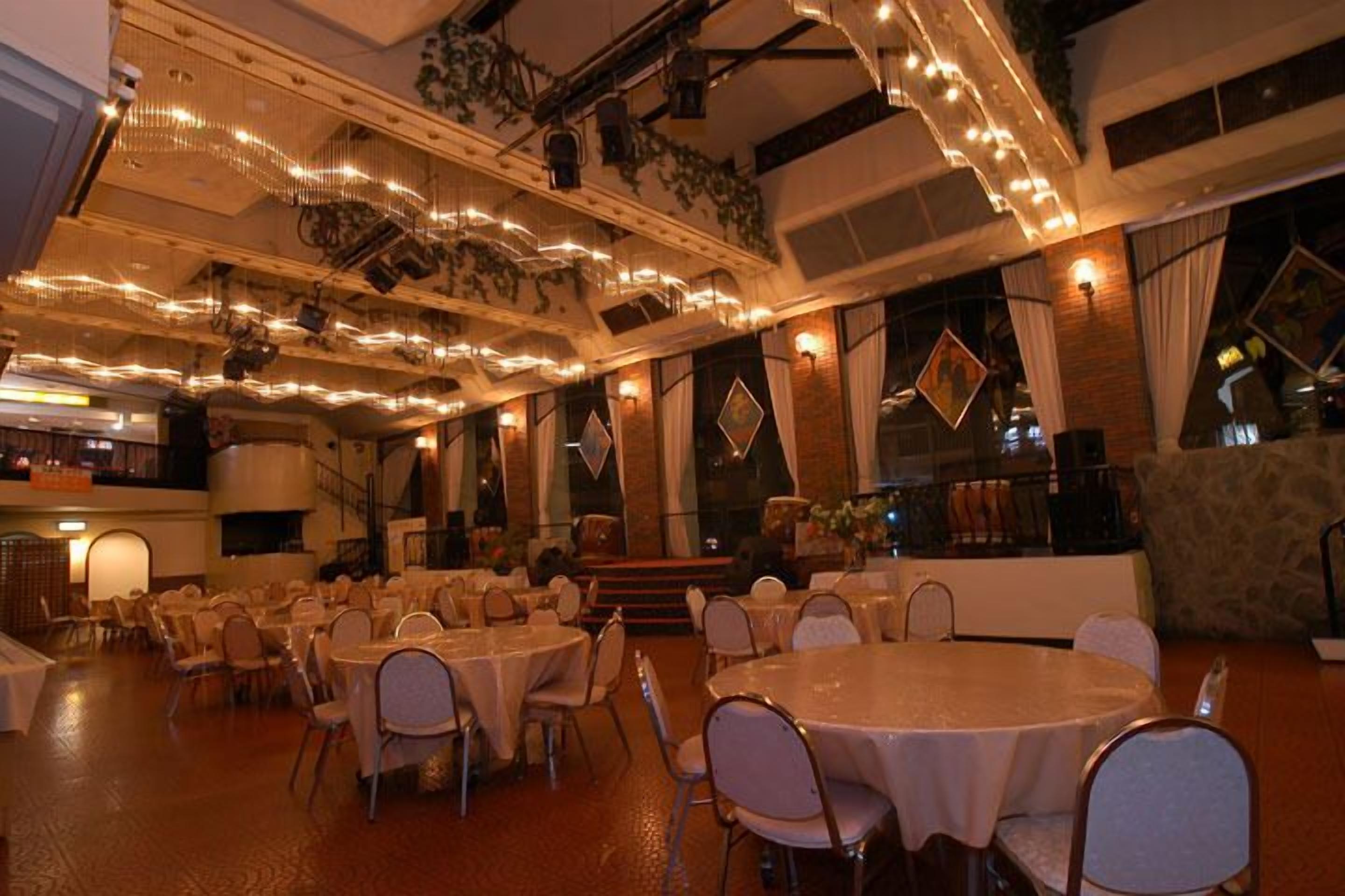 A banquet hall with round tables and chairs, chandeliers, and a stage.
