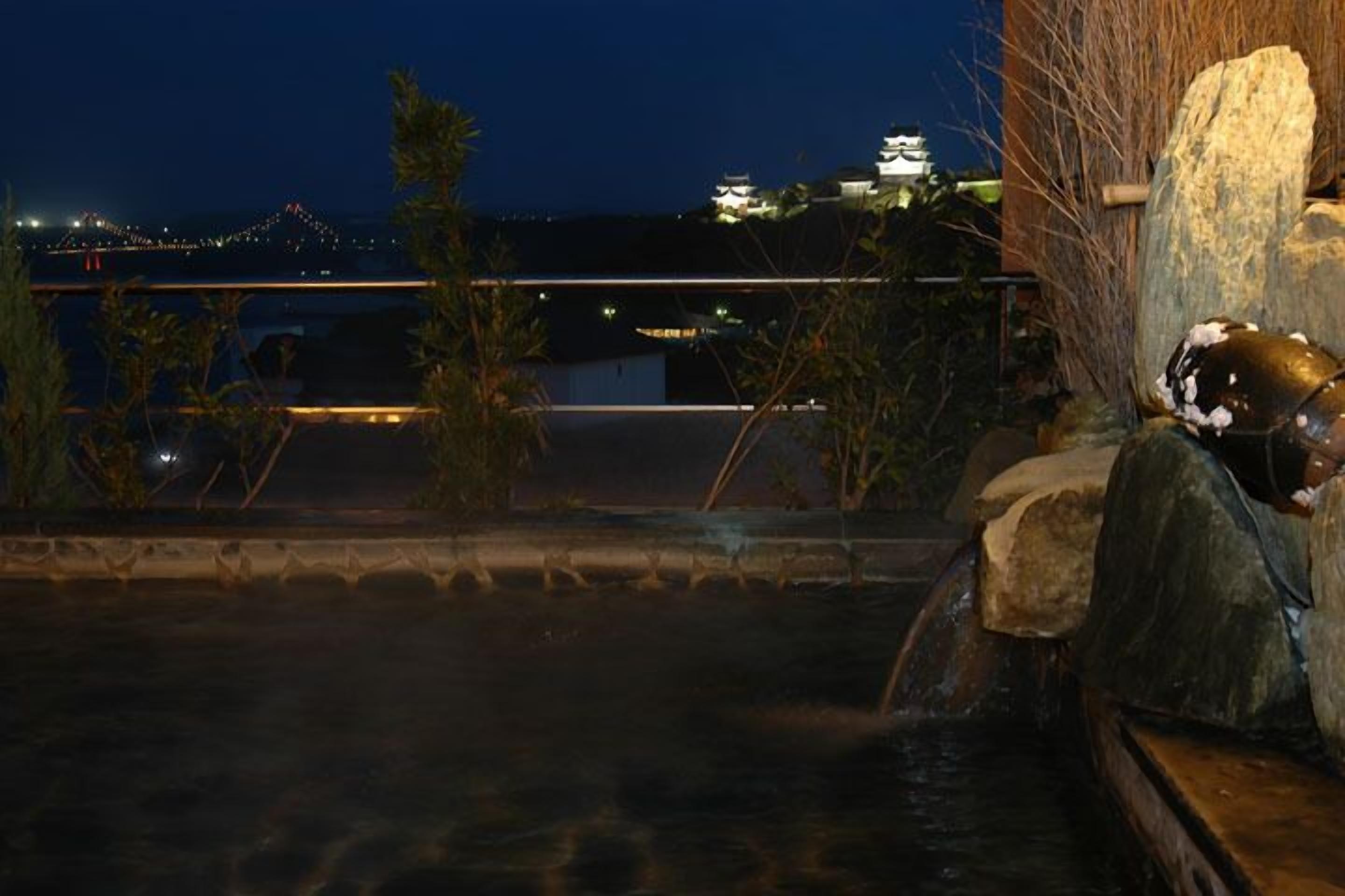 Vista noturna de uma construção tradicional japonesa com um elemento aquático em primeiro plano.