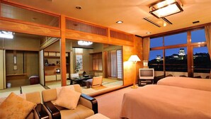 Habitación de hotel con una cama grande, un sofá, un televisor y vistas de un castillo a través del ventanal.