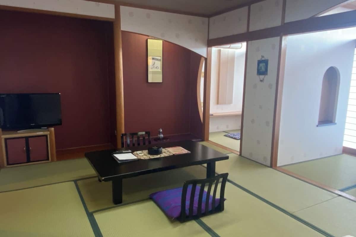 A traditional Japanese room with tatami flooring, a low table, chairs, a television, and sliding doors.