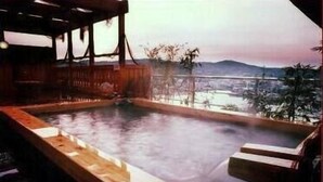 Baño de aguas termales con una terraza de madera y vistas a la ciudad y montañas.