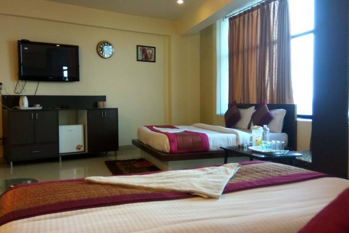 Una habitación de hotel con una cama, un escritorio, un televisor y un ventanal con cortinas.