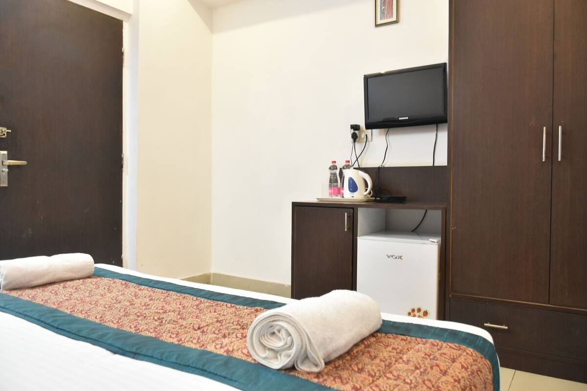 Habitación de hotel con cama, televisor montado en la pared, minibar y armario.