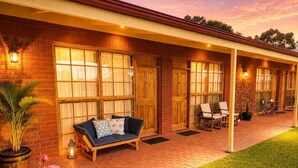 A covered outdoor seating area with a sofa and chairs, a brick wall, and a well-maintained lawn. - Coonawarra Place Motor Inn (Coonawarra)