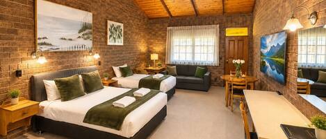 Habitación de hotel con pared de ladrillo, techo de madera, dos camas, un sofá, una mesa de comedor y obras de arte.