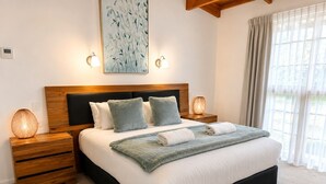 A bedroom with a large bed, two bedside tables, a headboard, and a painting on the wall. - Coonawarra Place Motor Inn (Coonawarra)