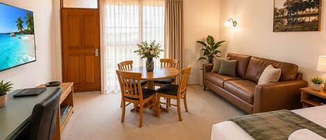 A cozy room with a wooden ceiling, a dining table with chairs, a sofa, a bed, a TV, and a painting on the wall.