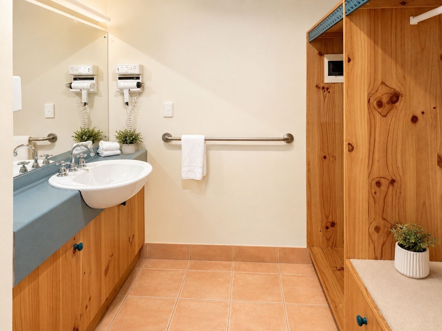 Une salle de bain équipée d’un lavabo, d’un miroir, d’un porte-serviettes et de deux sèche-cheveux fixés au mur.