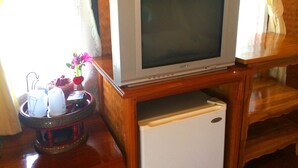 Un téléviseur posé sur un meuble en bois, un petit réfrigérateur en dessous, et un plateau avec des tasses et un vase de fleurs.