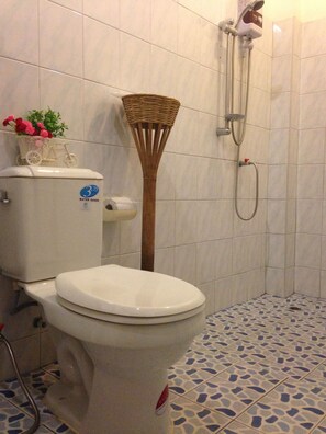 Um banheiro com vaso sanitário, dispositivo economizador de água, chuveiro e piso estampado.