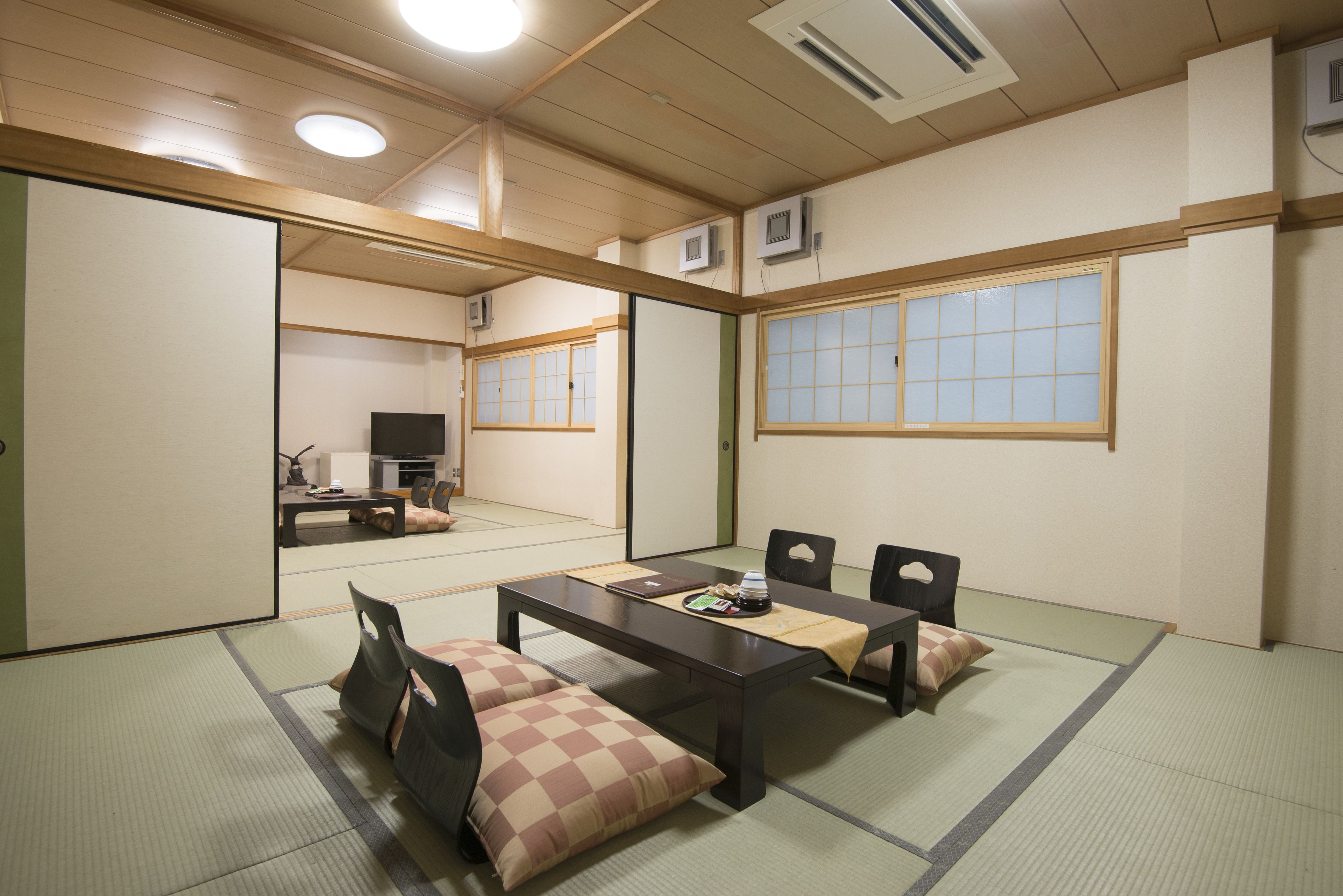 Una tradizionale stanza giapponese con pavimento in tatami, un tavolino, sedie e una televisione sullo sfondo.