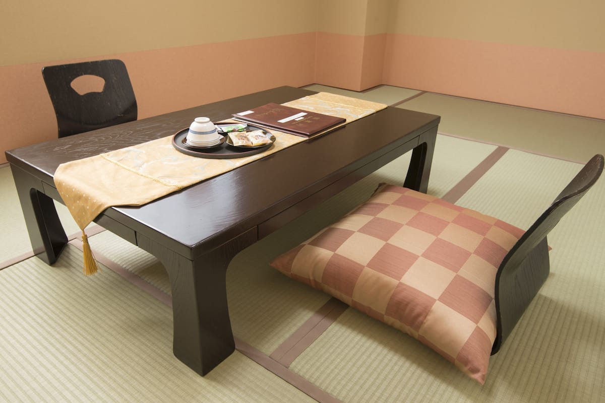 Ein traditioneller japanischer Raum mit Tatami-Böden, einem niedrigen Tisch mit Kissen und einem schwarzen Sessel.