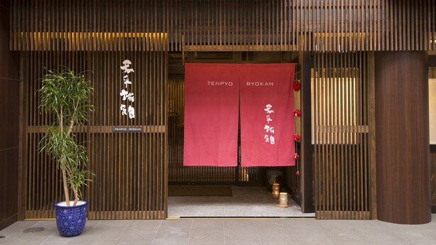 Ein traditioneller japanischer Eingang mit Holzlamellen und roten Bannern mit weißer Schrift.