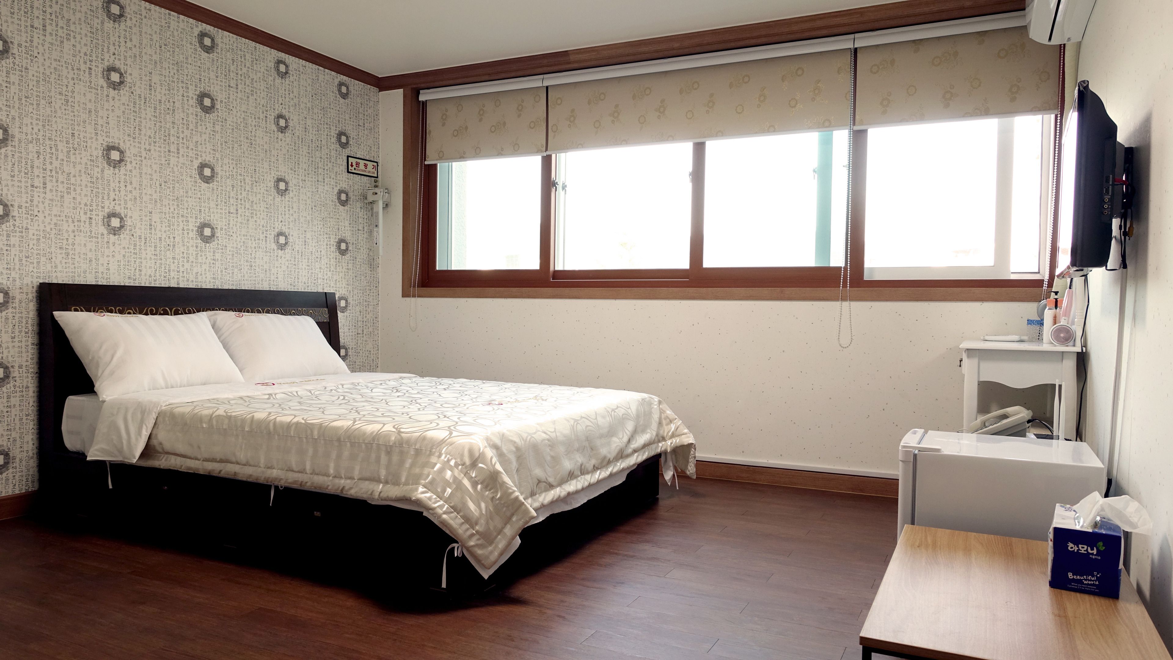 Ein Schlafzimmer mit Bett, Fenster, Nachttisch und einem an der Wand befestigten Fernseher.