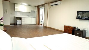 A hotel room with a bed, a small desk, a dresser, an air conditioning unit, and a kitchen area with cabinets and a sink. - Happy Memory (Jeonju)