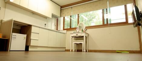 A spacious room with a large window, a white vanity with a mirror, and a refrigerator.