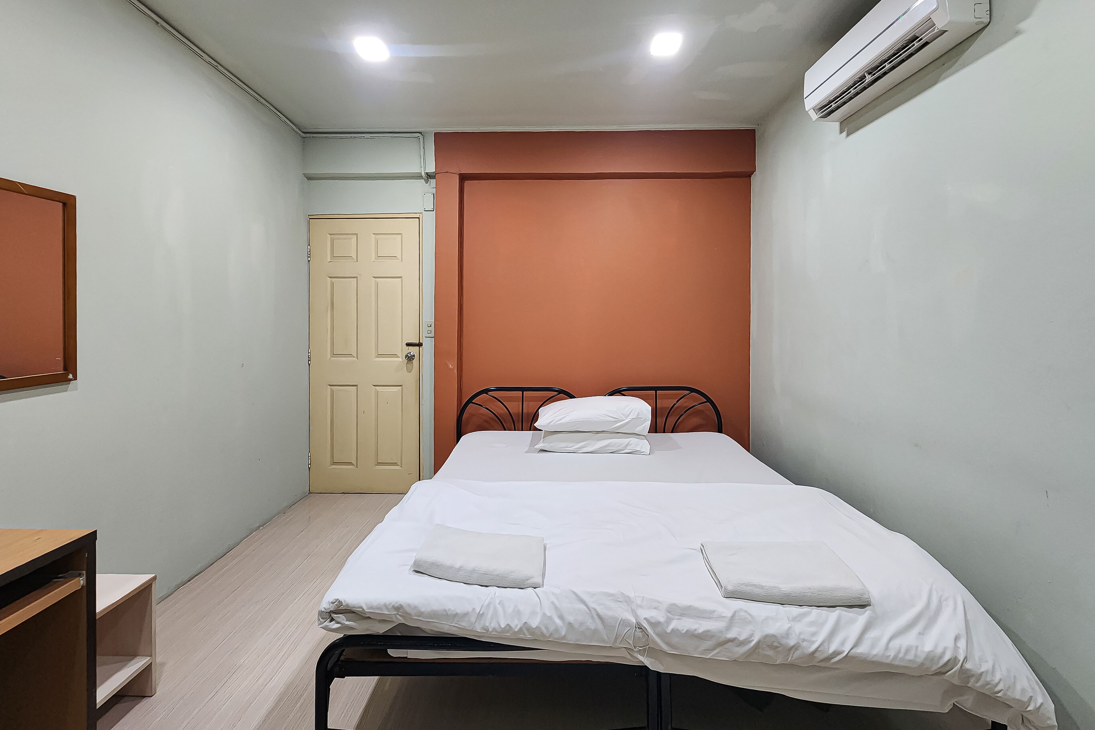 A small, neatly arranged bedroom with a single bed, a bedside table, and an air conditioning unit mounted on the wall.