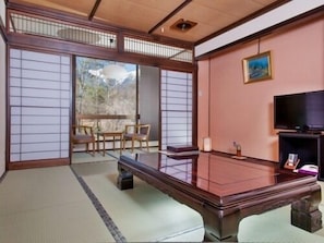 A traditional Japanese room with tatami flooring, a low table, a television, and a view of mountains through shoji screens. - Hotel Yamabuki (Komagane)
