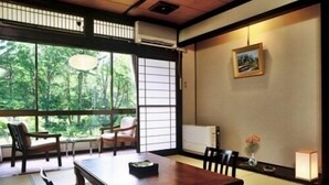 Une pièce de style japonais traditionnel, avec un sol recouvert de tatamis, une petite table en bois et une vue sur la verdure grâce à de grandes fenêtres.