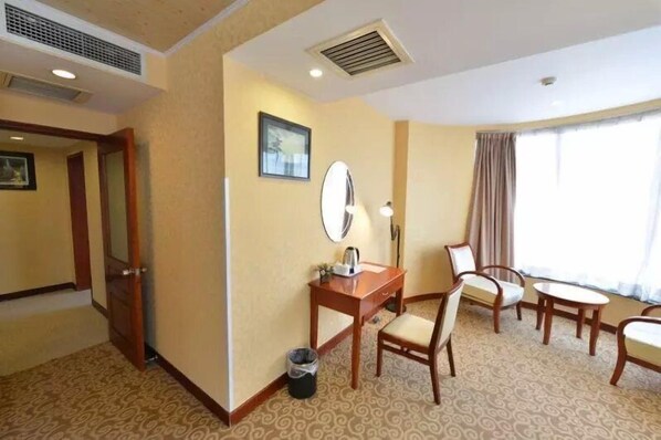 Una habitación de hotel con escritorio, silla y un amplio ventanal con cortinas.
