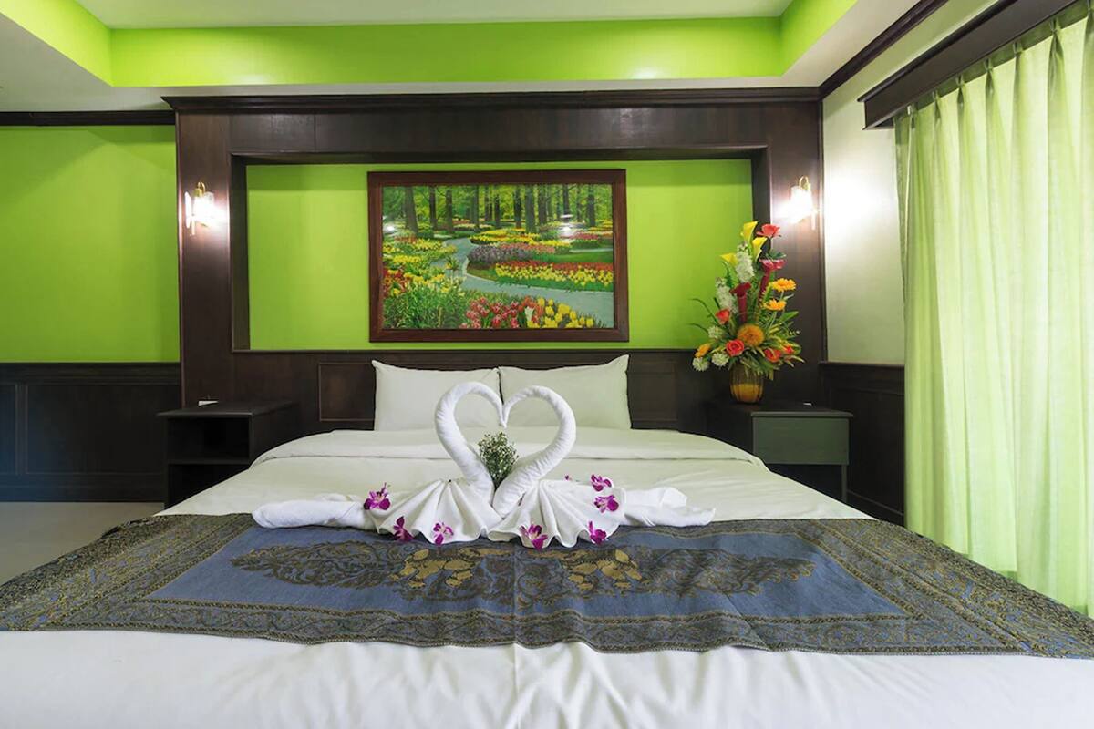 A hotel room with a bed, green walls, a painting of a garden, and a bouquet of flowers.