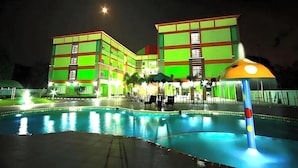 Un hotel con zona de piscina, varias plantas y una fachada iluminada durante la noche.