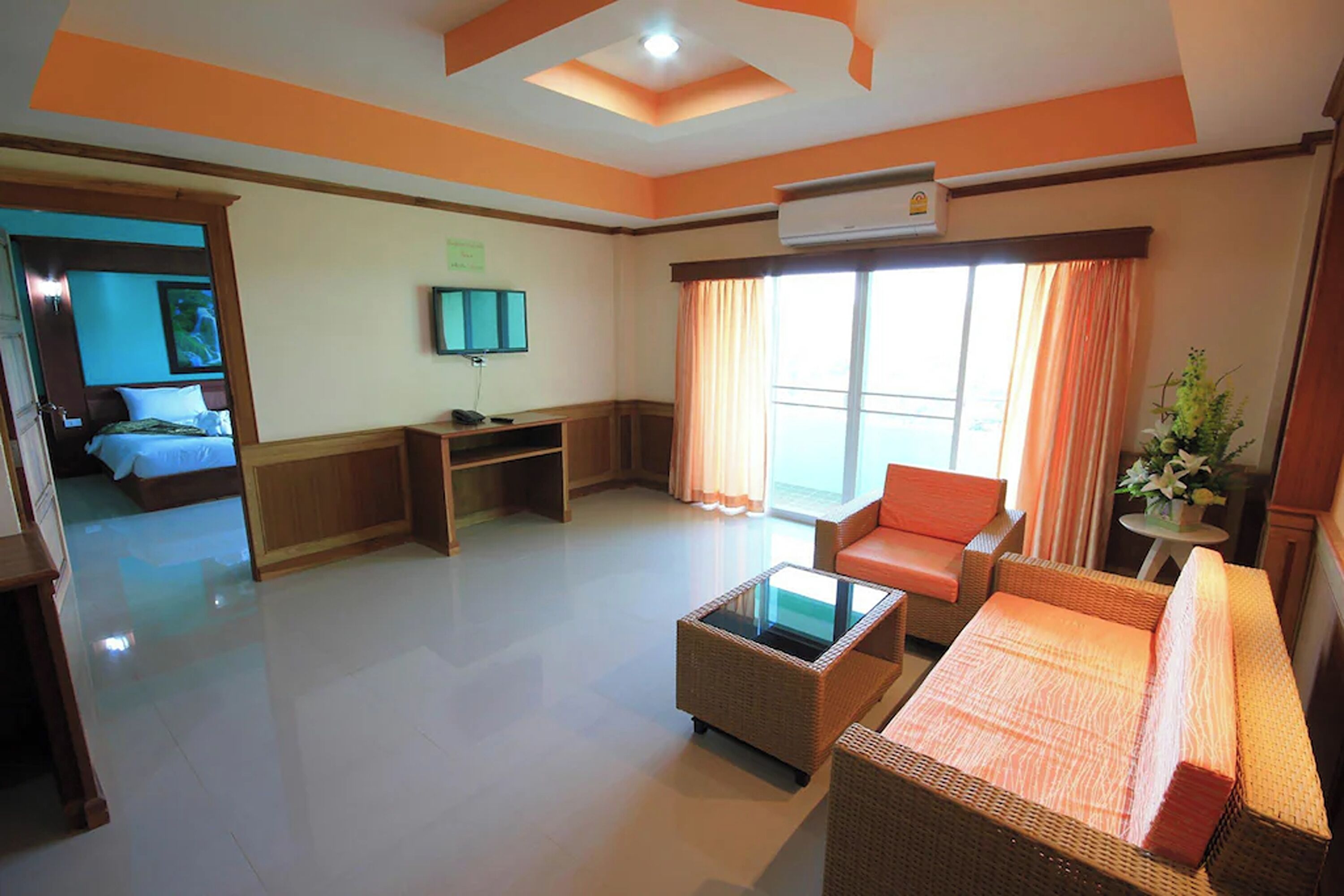 A hotel room with a bed, a sofa, a coffee table, a TV, and a window with curtains.