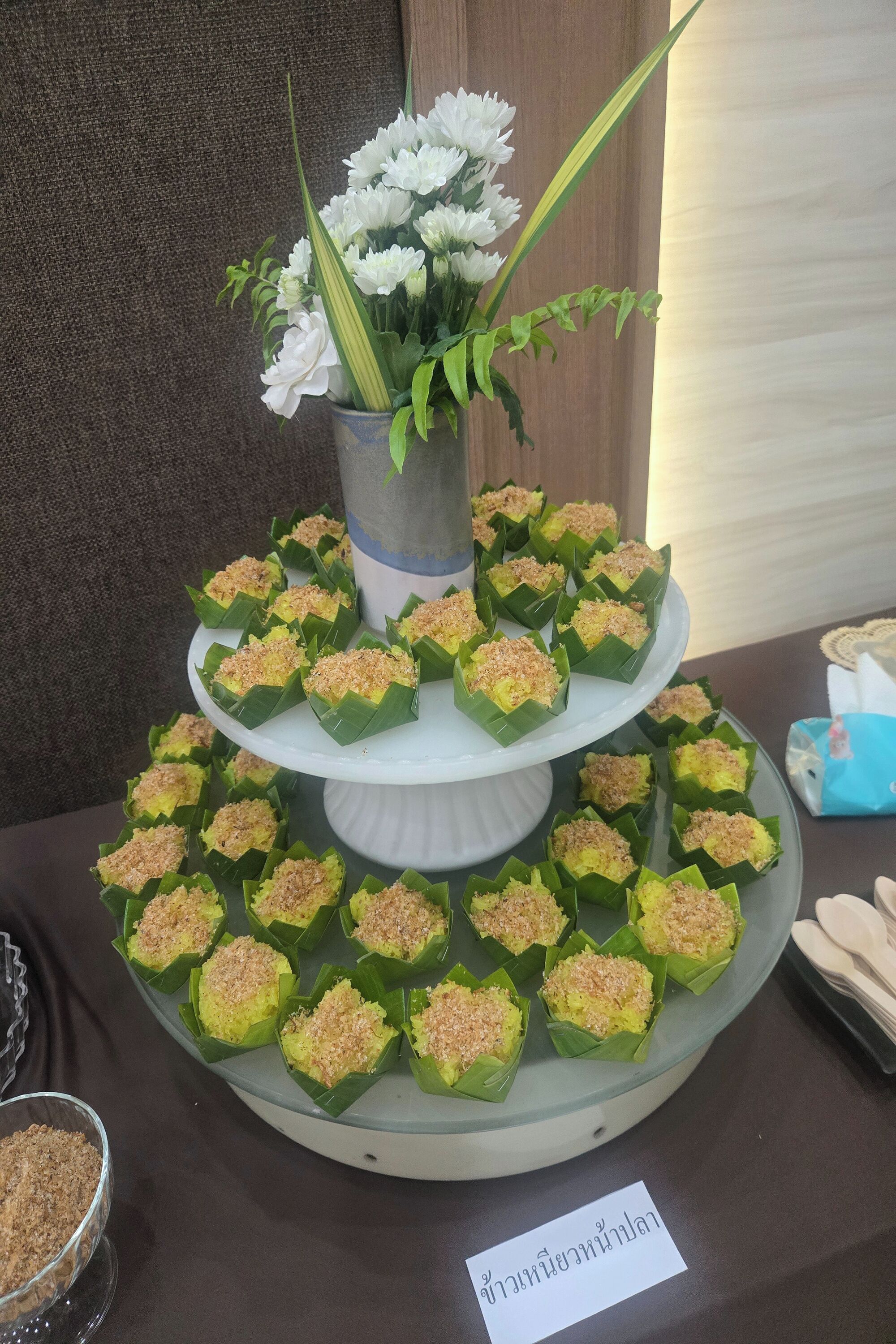 Une table sur laquelle sont présentés des desserts disposés en étages, un vase rempli de fleurs blanches et un panneau avec du texte.