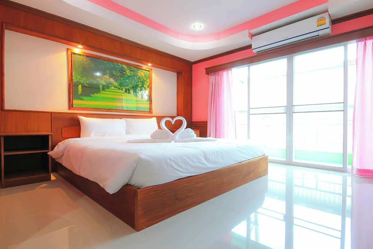 A hotel room with a large bed, a painting on the wall, and a window with curtains.