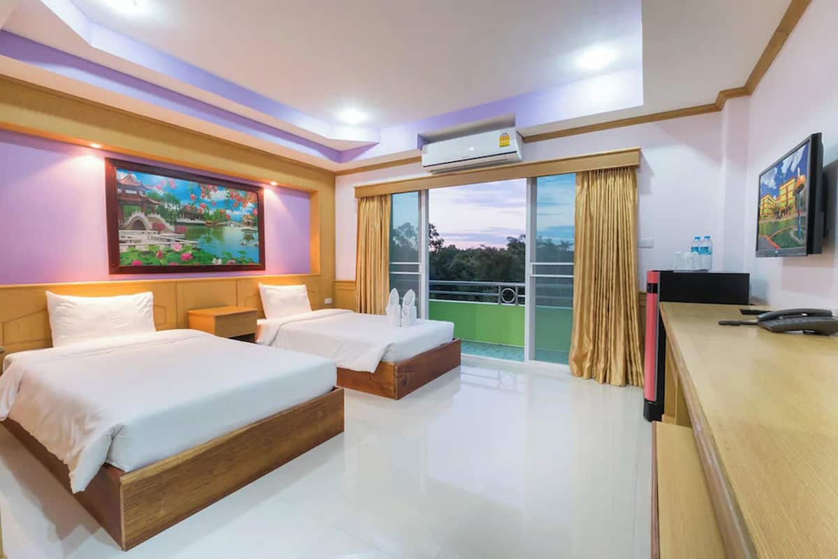 A hotel room with two beds, a balcony with a view, a painting on the wall, and a desk with a phone and water bottles.