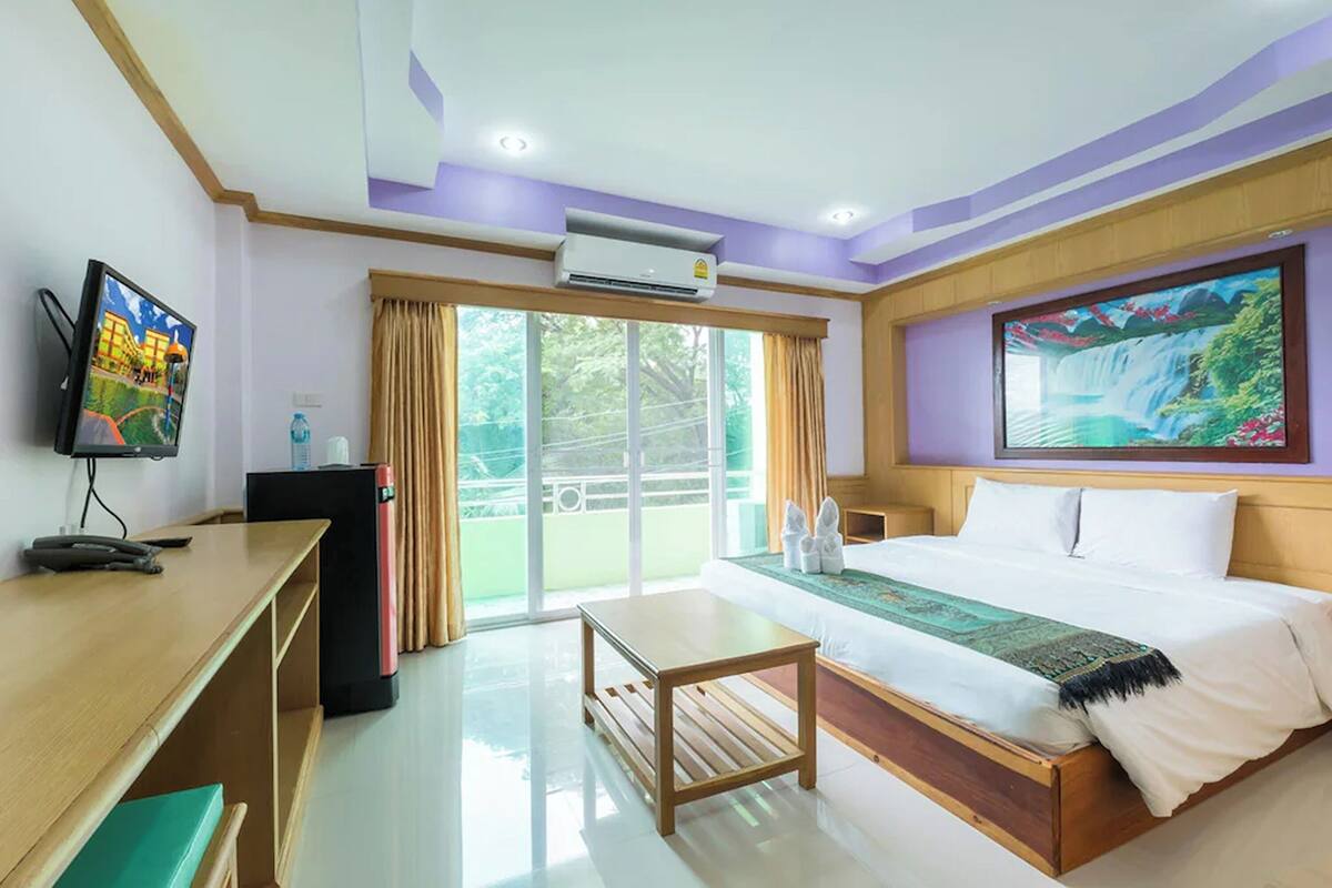 A hotel room with a bed, a desk, a television, an air conditioner, and a large window.