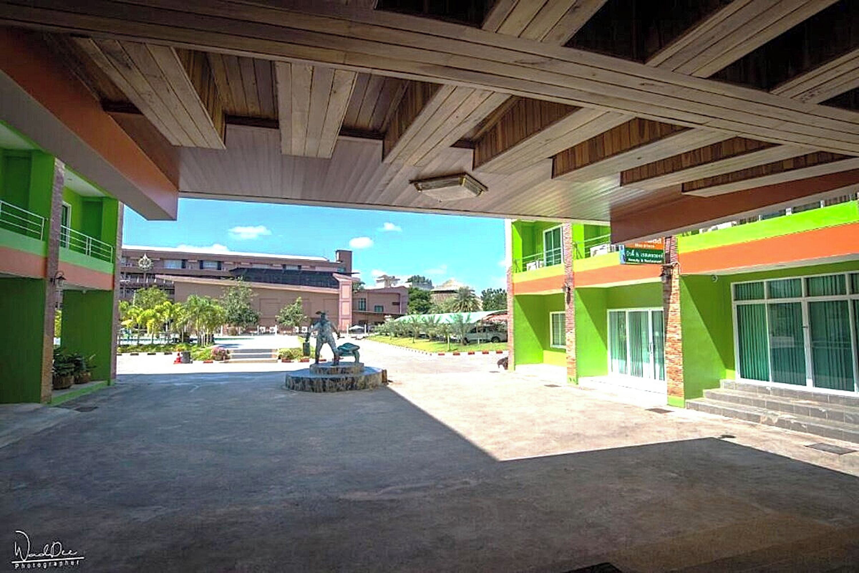 A spacious courtyard with a statue, green buildings, and a clear sky.