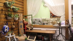 A room with wooden paneling, a wooden bench, a small stool, a table with a sign, and various potted plants. - Snail Trail B&B (Taitung)
