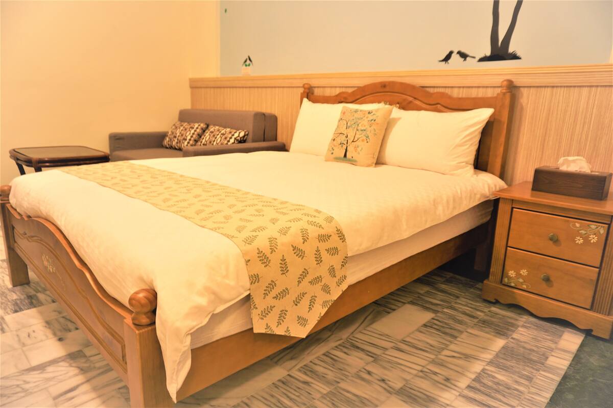 A neatly made bed with a patterned bedspread, a bedside table with a tissue box, and a nightstand with drawers.