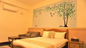 A neatly made bed with a wooden headboard, a nightstand with a tissue box, a small table, and a sofa with patterned cushions. - Snail Trail B&B (Taitung)