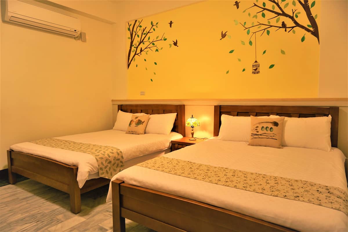 Two single beds with wooden frames, a wall-mounted air conditioner, and a wall decoration of birds and a hanging lantern.