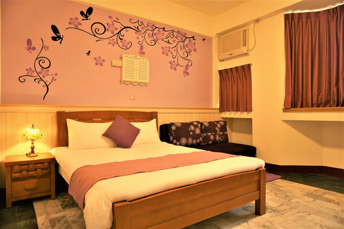 A neatly made bed with a wooden headboard, a nightstand with a lamp, and a decorative wall with floral and butterfly decals.