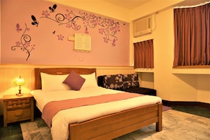 A neatly made bed with a wooden headboard, a nightstand with a lamp, and a decorative wall with floral and butterfly decals. - Snail Trail B&B (Taitung)