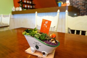 A small, white ceramic planter with green trim and a label, containing various succulents and a small figurine of a dog. - Snail Trail B&B (Taitung)