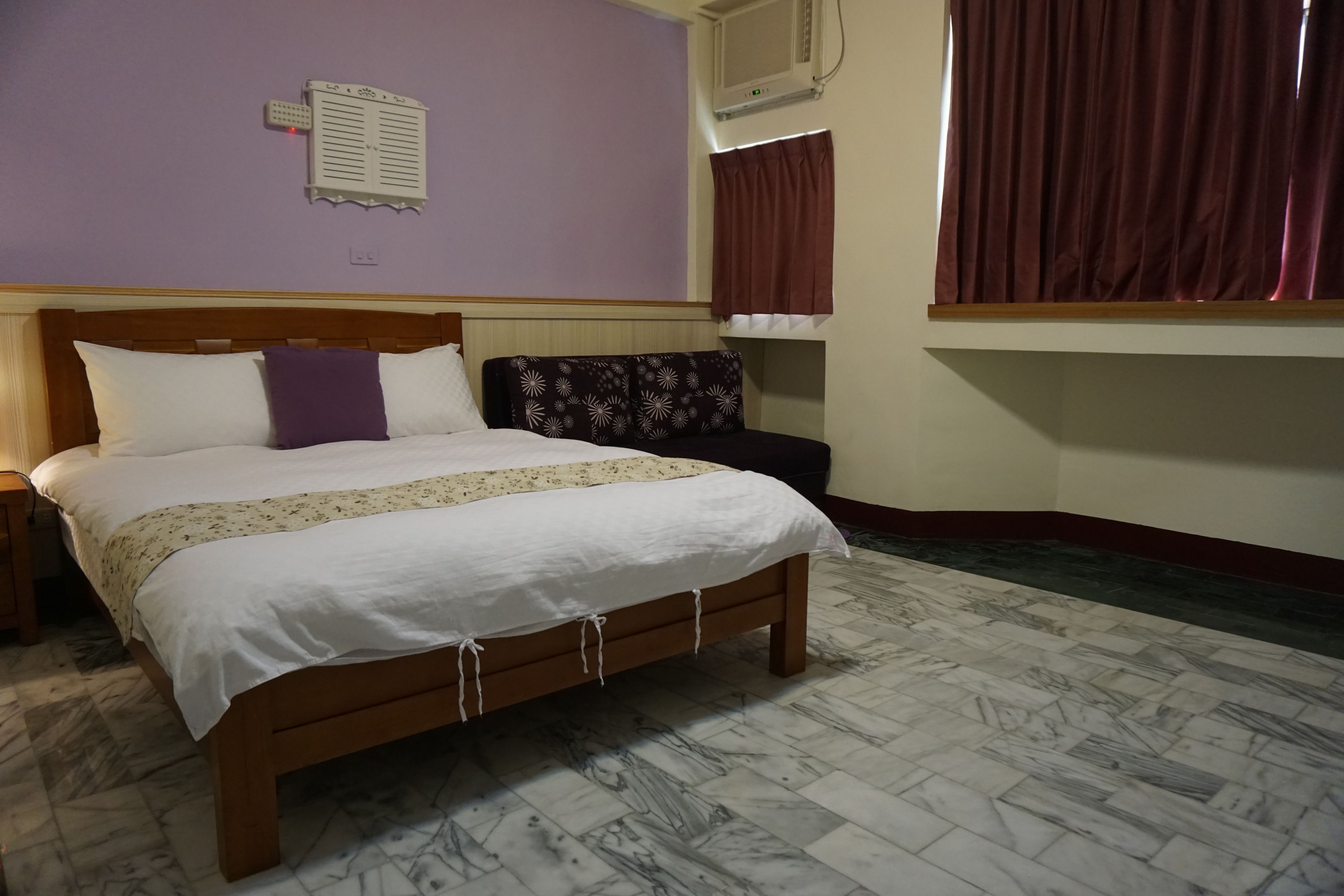 A bedroom with a wooden bed, a nightstand, a wall-mounted air conditioner, and a window with curtains.