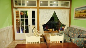 A room with a wooden dining table, two white chairs, a floral sofa, and a window with curtains. - Snail Trail B&B (Taitung)