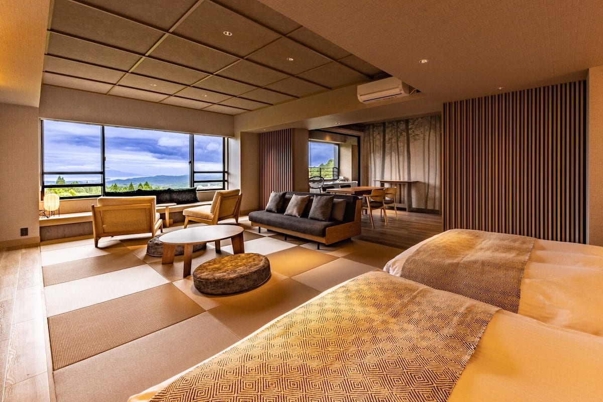 Habitación de hotel con una cama grande, un sofá, una mesa de comedor y vistas a las montañas.