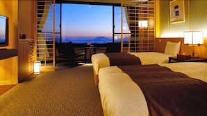 A hotel room with two beds, a TV, a desk, and a view of the mountains. - Kirishima Kanko Hotel (Kirishima)