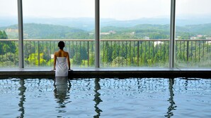 A person standing in a pool with a view of a forested landscape through large windows. - Kirishima Kanko Hotel (Kirishima)