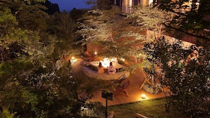 A circular outdoor seating area with a fire feature, surrounded by lush greenery and wooden deck flooring. - Kirishima Kanko Hotel (Kirishima)
