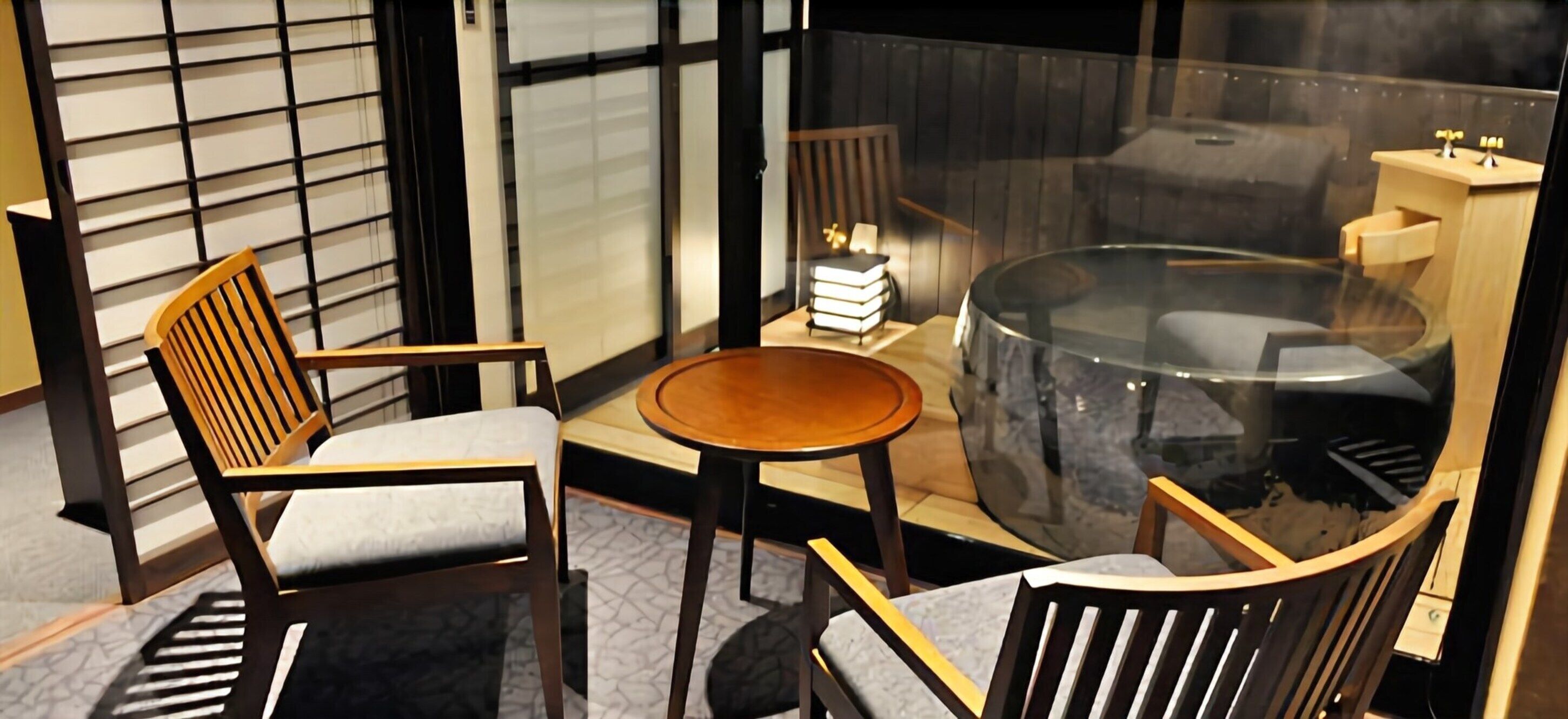 A modern room with a glass table, two wooden chairs, a small round table, and a bookshelf with books.