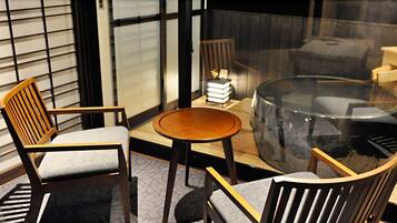 A modern room with a glass table, two wooden chairs, a small round table, and a bookshelf with books.