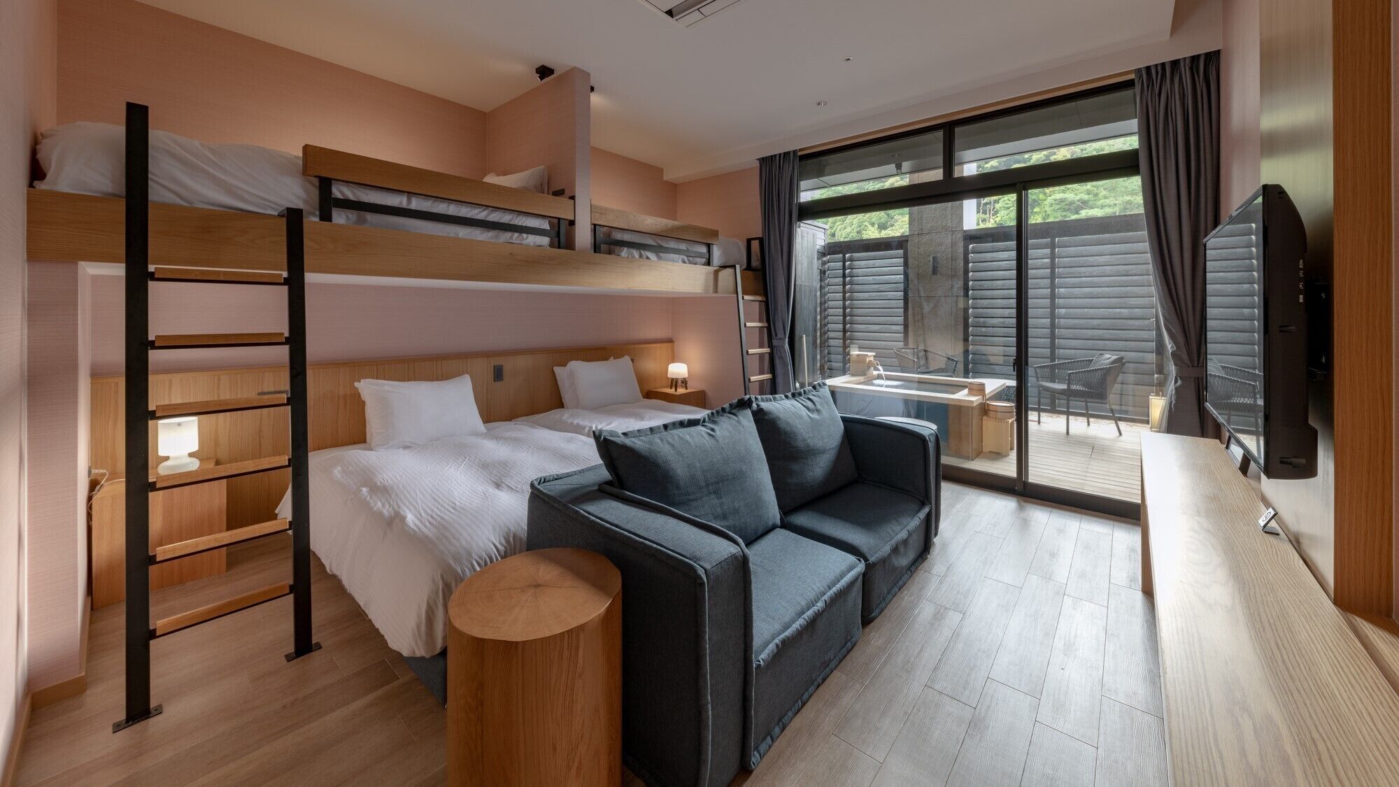 A modern hotel room with a bunk bed, a sofa, a small table, and a large window.