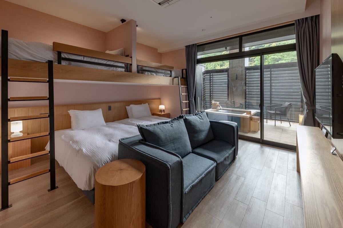 Une chambre d’hôtel moderne avec un lit superposé, un canapé, une petite table et une grande fenêtre.