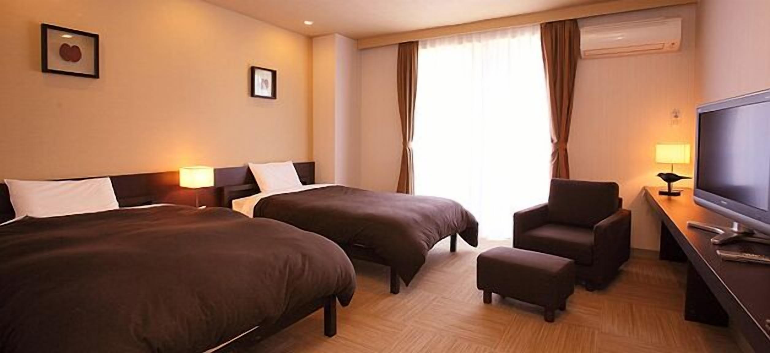 Ein Hotelzimmer mit zwei Betten, einem Schreibtisch mit Fernseher und einem Sessel.